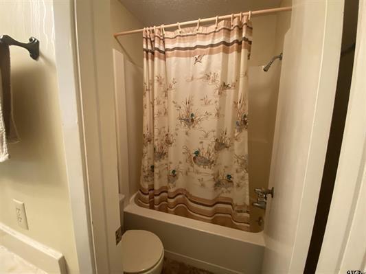 bathroom with toilet and shower / bath combination with curtain