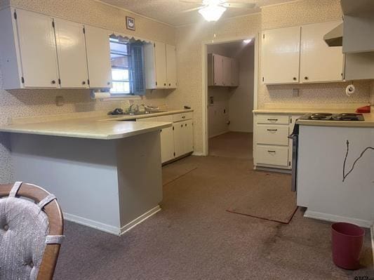 kitchen with ceiling fan, a peninsula, white cabinets, and gas stove