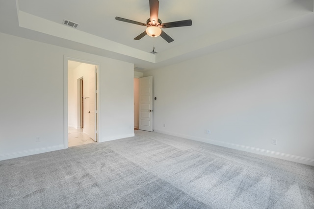 unfurnished room with ceiling fan, a tray ceiling, visible vents, light carpet, and baseboards