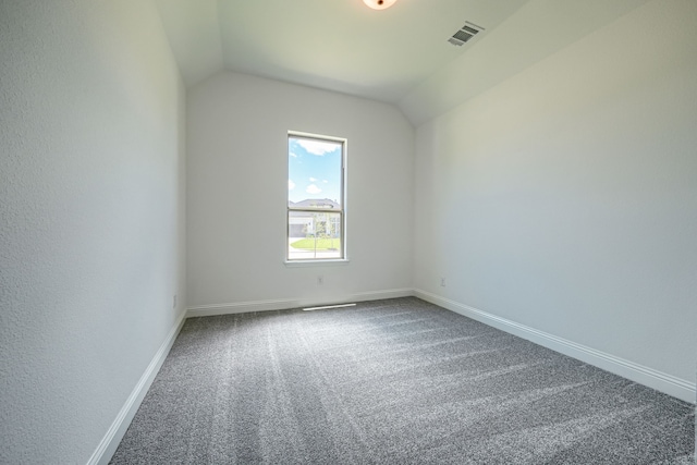 carpeted spare room with visible vents, vaulted ceiling, and baseboards