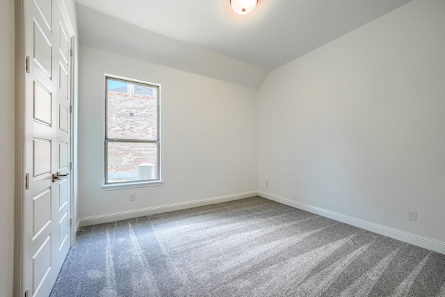 carpeted empty room featuring baseboards and vaulted ceiling