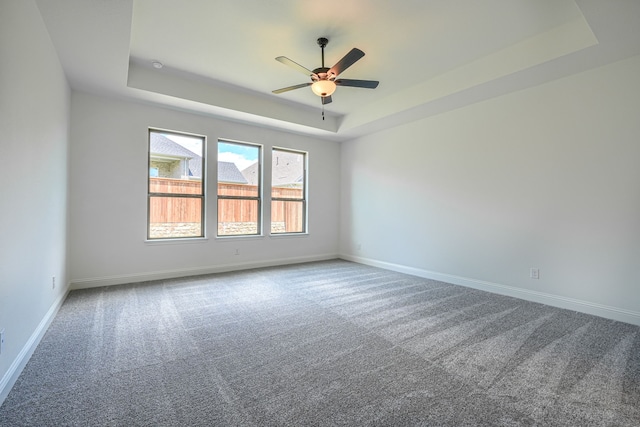 carpeted empty room with baseboards, a ceiling fan, and a tray ceiling