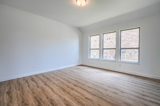 empty room with baseboards, wood finished floors, and vaulted ceiling