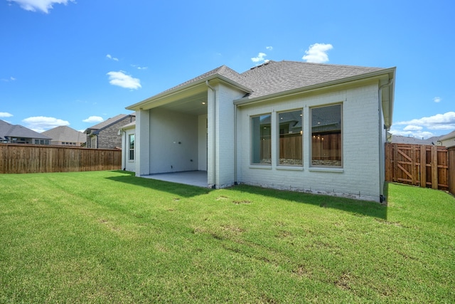 rear view of house with a fenced backyard, a yard, brick siding, a patio, and roof with shingles