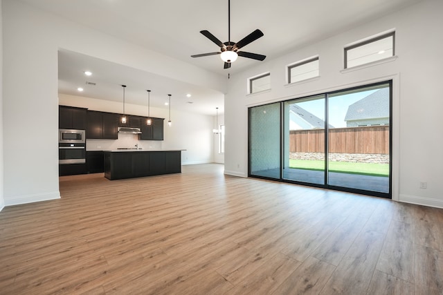 unfurnished living room featuring recessed lighting, ceiling fan, baseboards, light wood-type flooring, and a towering ceiling