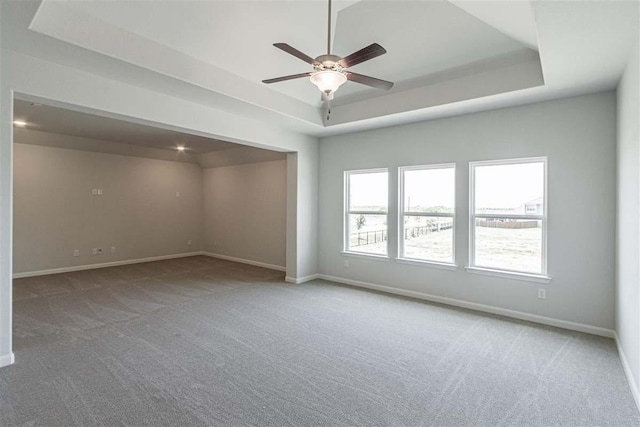 carpeted empty room featuring ceiling fan, a raised ceiling, and baseboards