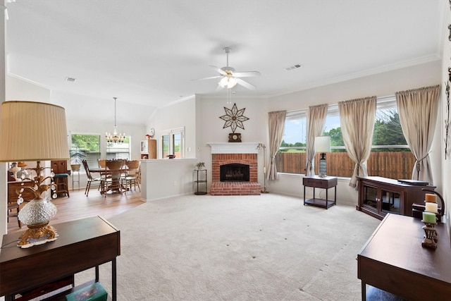 living room featuring a brick fireplace, crown molding, visible vents, baseboards, and ceiling fan with notable chandelier