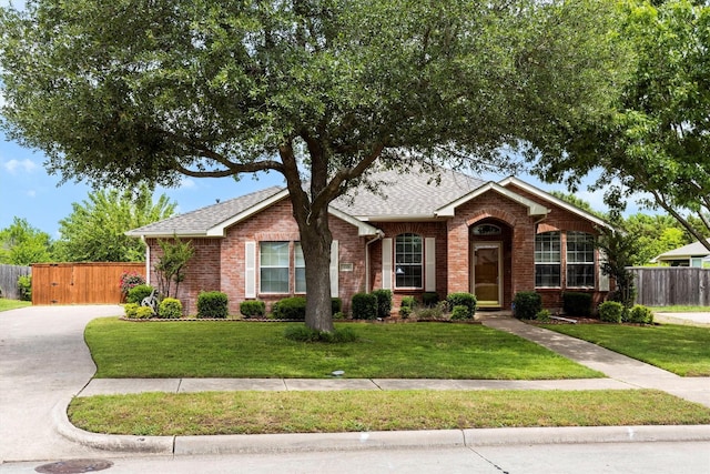 ranch-style home featuring brick siding, fence, a front yard, and roof with shingles