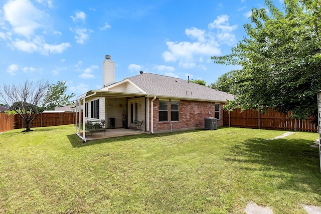 rear view of house featuring a chimney, a fenced backyard, a yard, brick siding, and a patio area