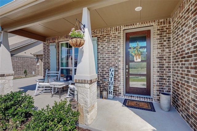 doorway to property with a porch and brick siding