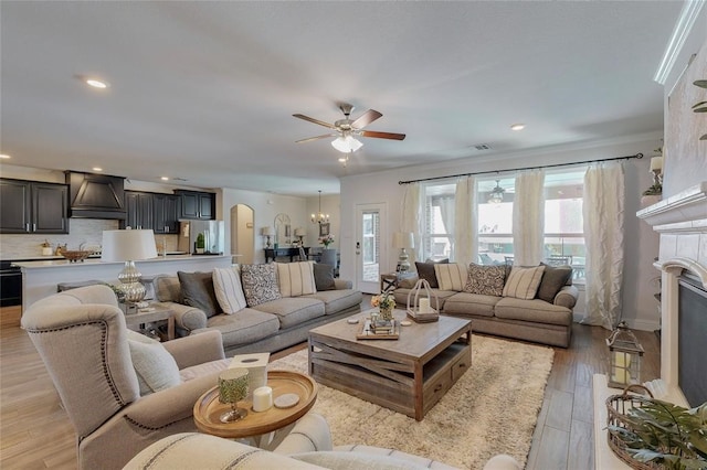 living room featuring ceiling fan, light wood-style floors, arched walkways, recessed lighting, and a tiled fireplace