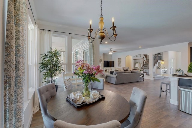 dining space with recessed lighting, arched walkways, wood finished floors, a wealth of natural light, and ceiling fan with notable chandelier