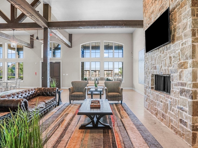 living area featuring baseboards, beam ceiling, a fireplace, a towering ceiling, and a ceiling fan