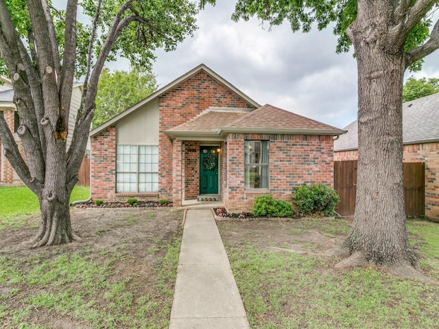 view of front facade with fence, roof with shingles, a front yard, and brick siding