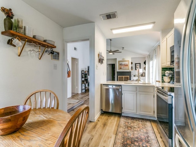 kitchen with light wood-style floors, appliances with stainless steel finishes, a sink, visible vents, and lofted ceiling with skylight