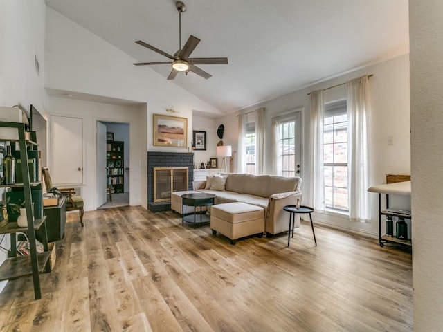 living room featuring a ceiling fan, high vaulted ceiling, light wood-style floors, and a fireplace