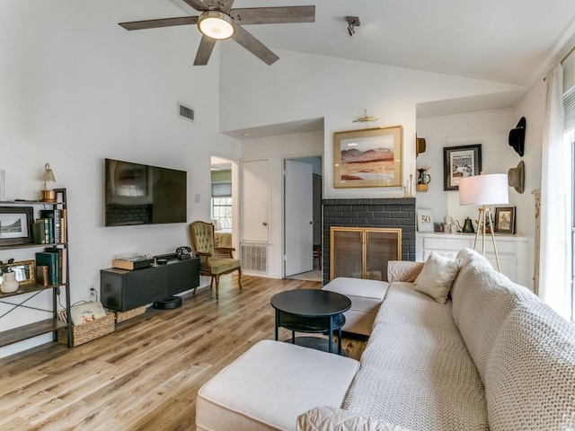 living room with visible vents, light wood-style floors, a brick fireplace, a ceiling fan, and high vaulted ceiling