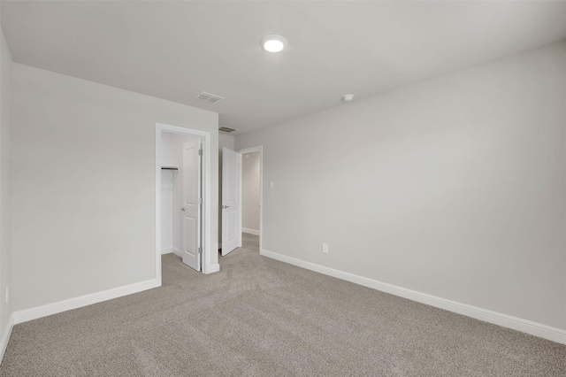 unfurnished bedroom featuring carpet, visible vents, baseboards, and a walk in closet