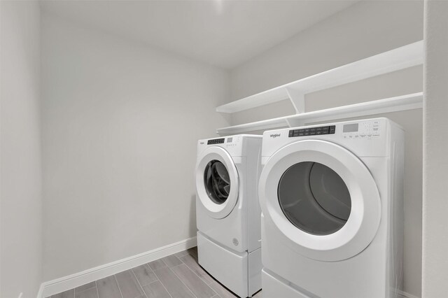 clothes washing area with baseboards, wood tiled floor, laundry area, and washing machine and dryer