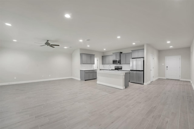 kitchen featuring gray cabinetry, open floor plan, stainless steel appliances, and baseboards