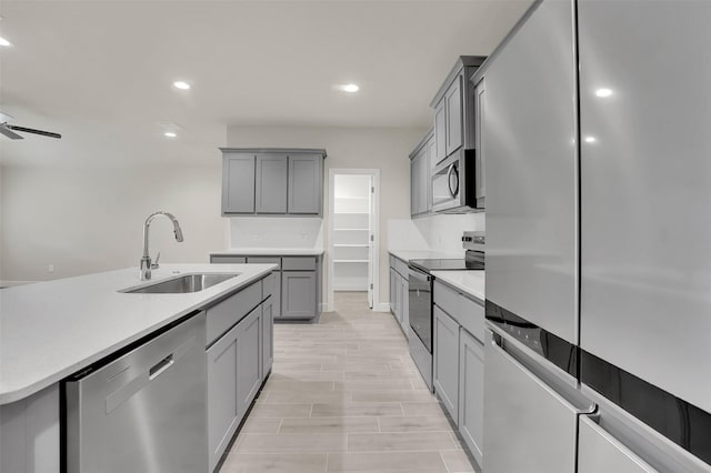 kitchen featuring gray cabinetry, a sink, appliances with stainless steel finishes, and light countertops