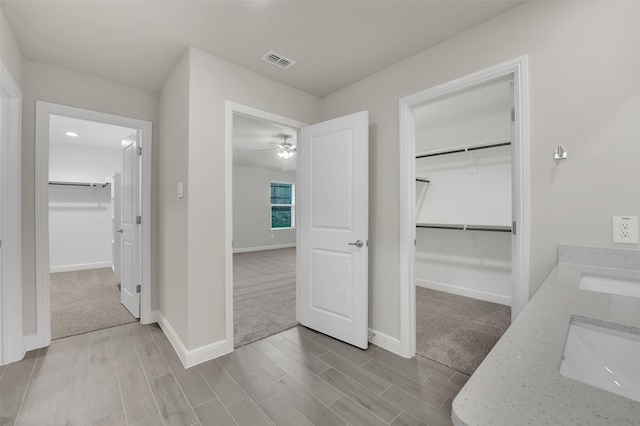 full bath with a walk in closet, a sink, baseboards, visible vents, and wood tiled floor