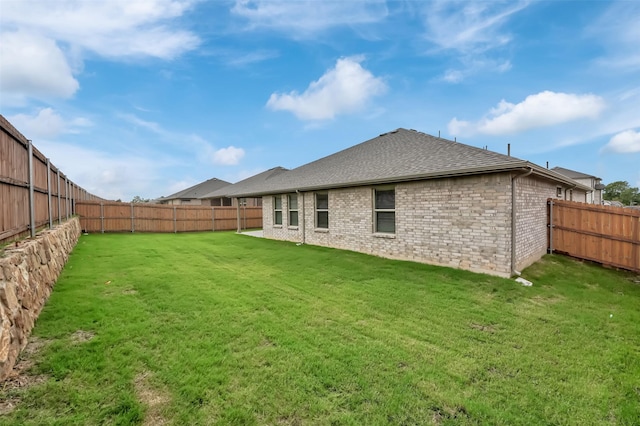 rear view of house with a yard, a shingled roof, brick siding, and a fenced backyard