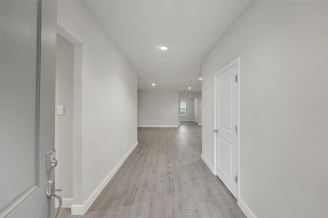 hallway featuring baseboards, recessed lighting, and light wood-style floors