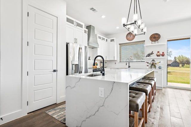 kitchen with wood finished floors, custom range hood, stainless steel fridge with ice dispenser, a kitchen bar, and visible vents