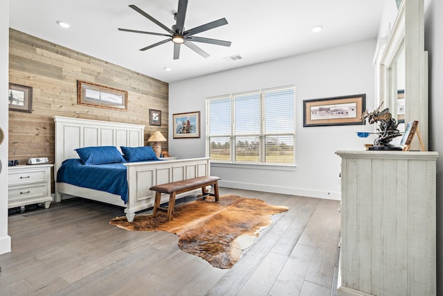 bedroom featuring an accent wall, baseboards, wooden walls, recessed lighting, and wood finished floors
