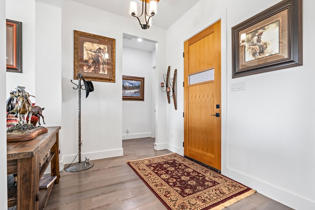 foyer featuring baseboards, visible vents, wood finished floors, and a chandelier
