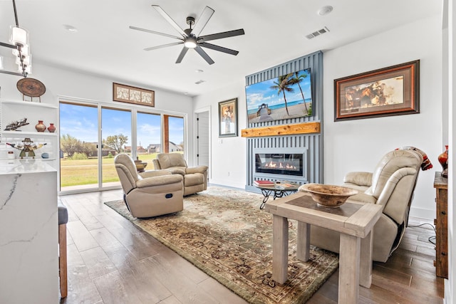 living room featuring hardwood / wood-style floors, a glass covered fireplace, visible vents, and a ceiling fan