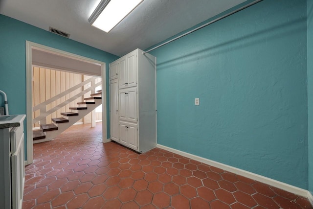 spare room with stairway, dark tile patterned floors, a sink, baseboards, and visible vents