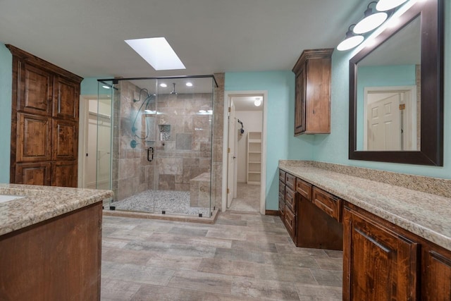 bathroom featuring a walk in closet, a skylight, a shower stall, and vanity