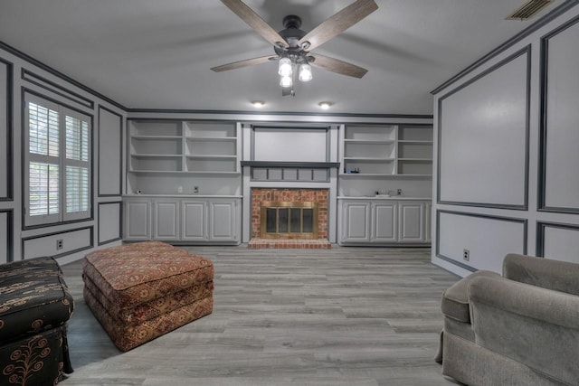 living area with visible vents, ceiling fan, light wood finished floors, a fireplace, and a decorative wall