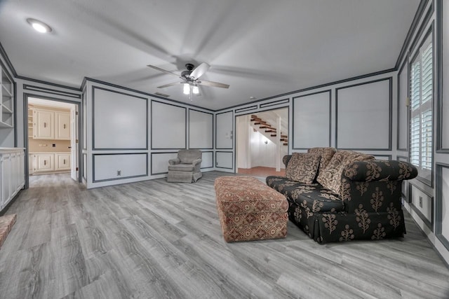 living room featuring light wood-style floors, a decorative wall, a ceiling fan, and stairs