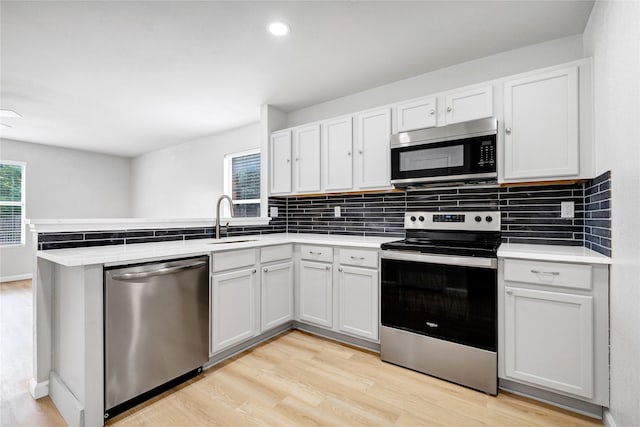kitchen featuring tasteful backsplash, a sink, light wood-style floors, stainless steel appliances, and a peninsula