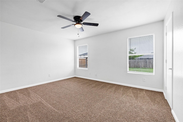 spare room with dark carpet, a ceiling fan, and baseboards