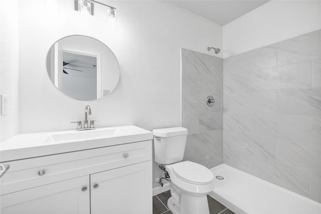 full bathroom featuring toilet, ceiling fan, tiled shower, and vanity