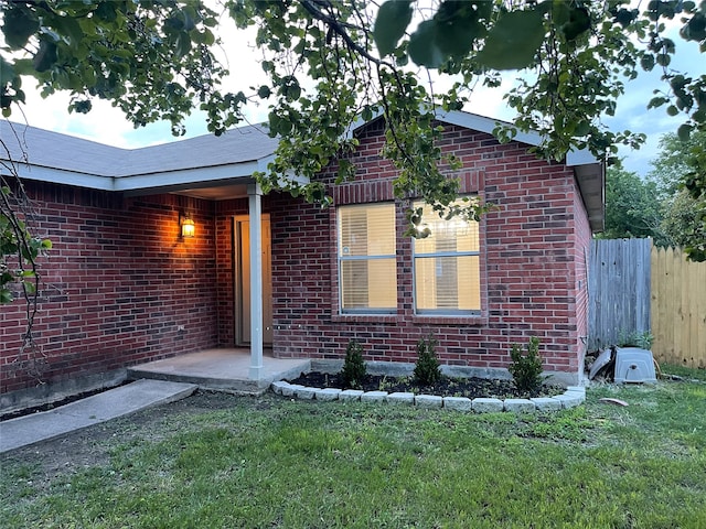 entrance to property with brick siding, fence, and a yard