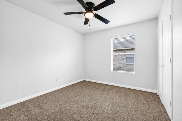 empty room with dark colored carpet, a ceiling fan, and baseboards