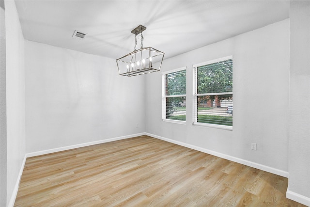 unfurnished dining area featuring an inviting chandelier, visible vents, light wood-style flooring, and baseboards