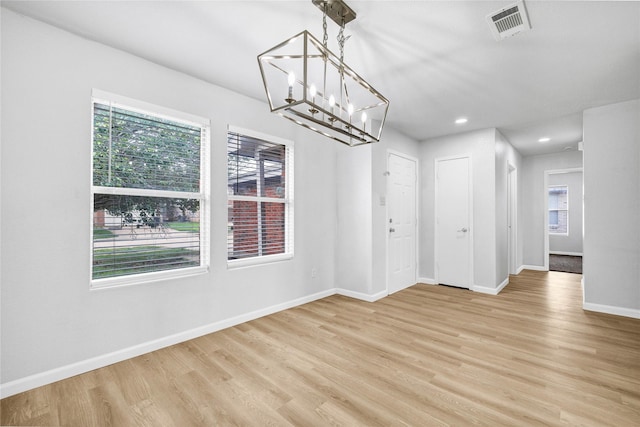 unfurnished dining area with an inviting chandelier, baseboards, light wood-style floors, and visible vents