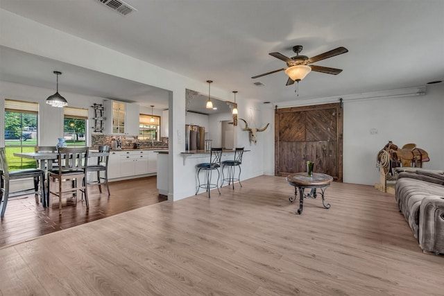 living room featuring light wood-style floors, a ceiling fan, a barn door, and visible vents