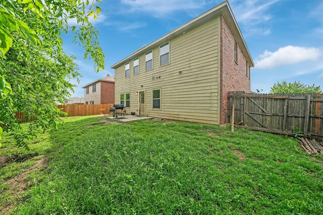 rear view of property with a patio, brick siding, a fenced backyard, and a yard