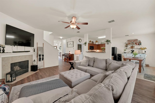 living room with a fireplace, wood finished floors, visible vents, and ceiling fan