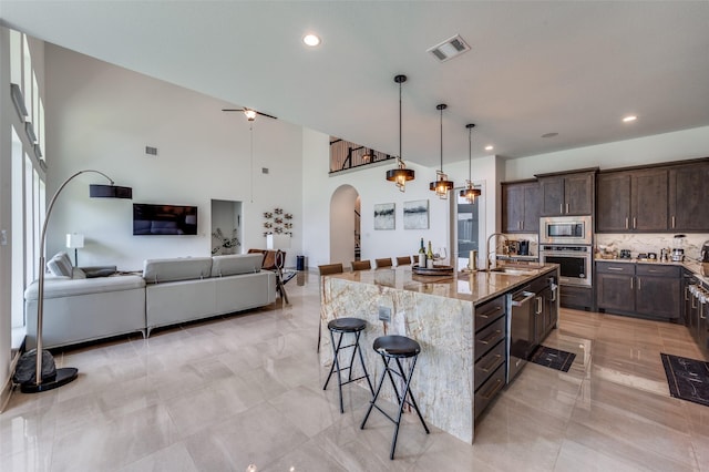 kitchen featuring a kitchen breakfast bar, a sink, stainless steel appliances, arched walkways, and light stone countertops