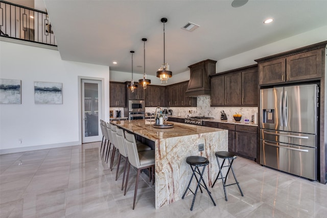 kitchen featuring a kitchen breakfast bar, light stone counters, appliances with stainless steel finishes, visible vents, and dark brown cabinetry