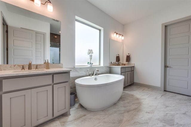 full bathroom with a freestanding tub, two vanities, marble finish floor, and a sink