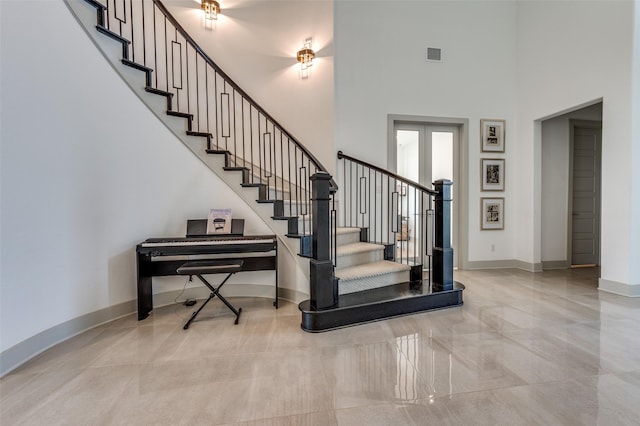 staircase with a high ceiling, visible vents, and baseboards